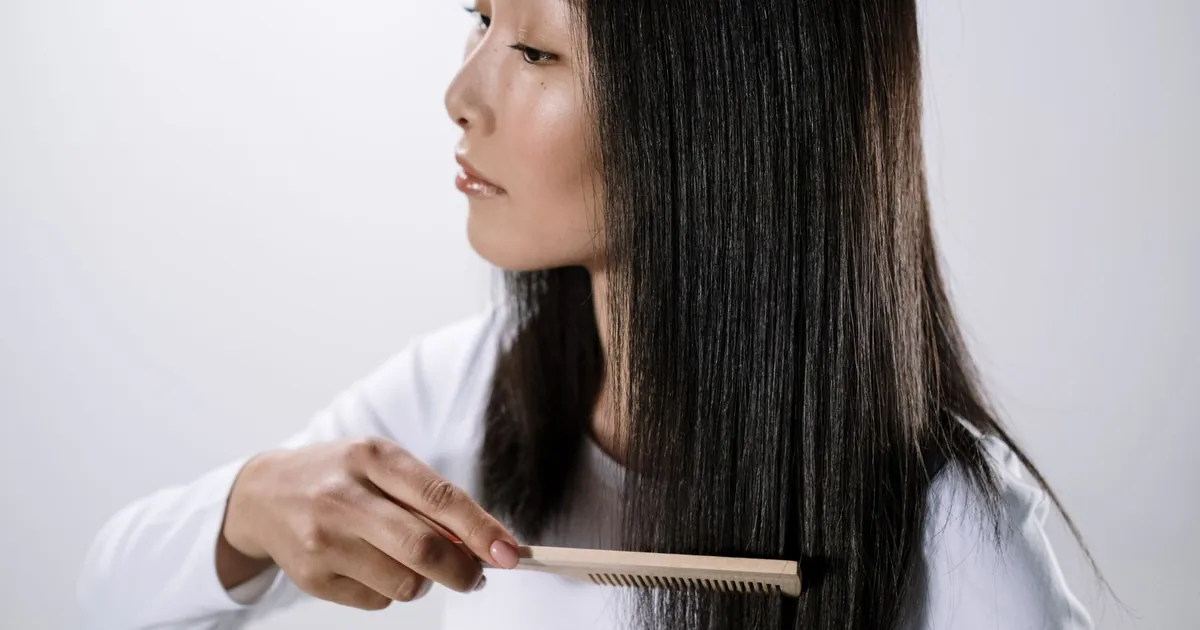 Portrait studio d'une femme asiatique peignant ses cheveux noirs lisses sur fond blanc.