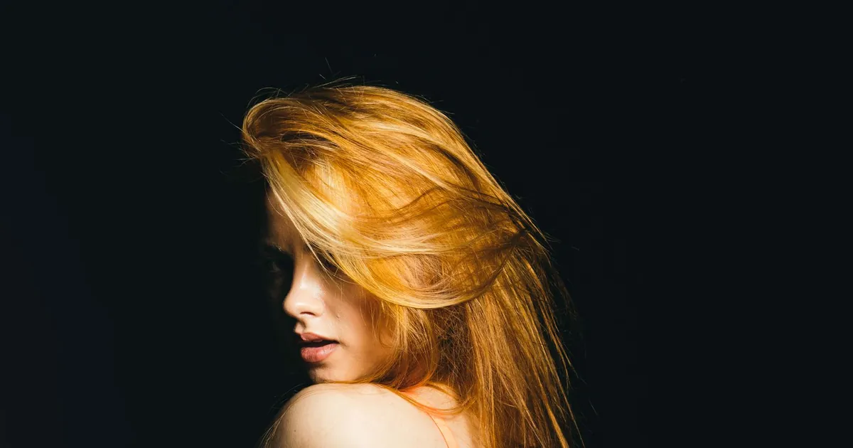 Femme rousse aux longs cheveux fluides sur fond noir dramatique
