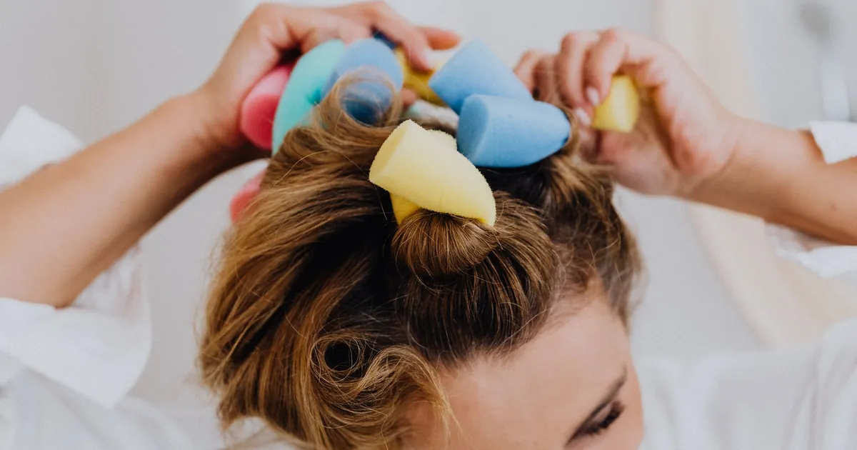 Gros plan d'une femme posant des bigoudis en mousse colorés dans ses cheveux.