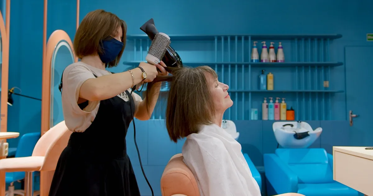 Coiffeur séchant les cheveux d'une femme âgée au salon chic.