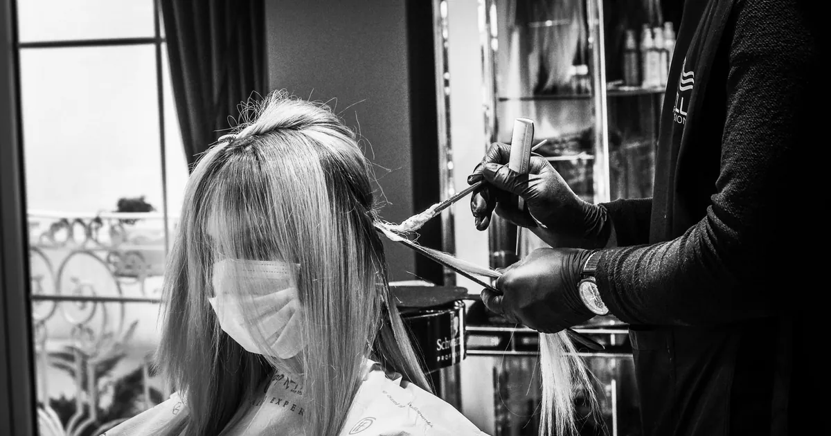 Coiffeuse appliquant une couleur à une cliente masquée, en noir et blanc