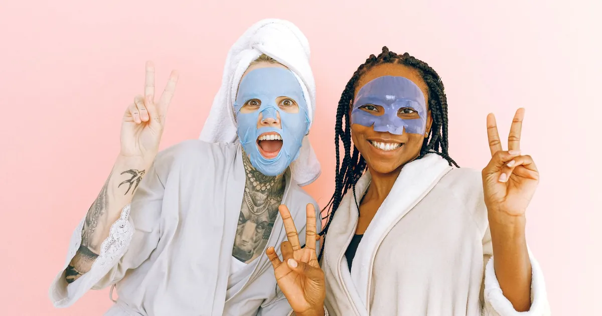 Deux femmes en peignoirs, masques de soin sur le visage, faisant des signes de paix.