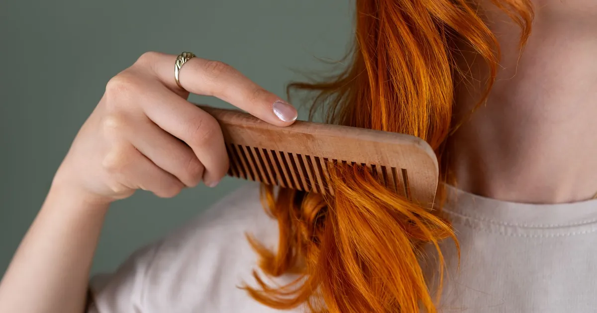 Gros plan d'une femme peignant ses cheveux roux bouclés avec un peigne en bois