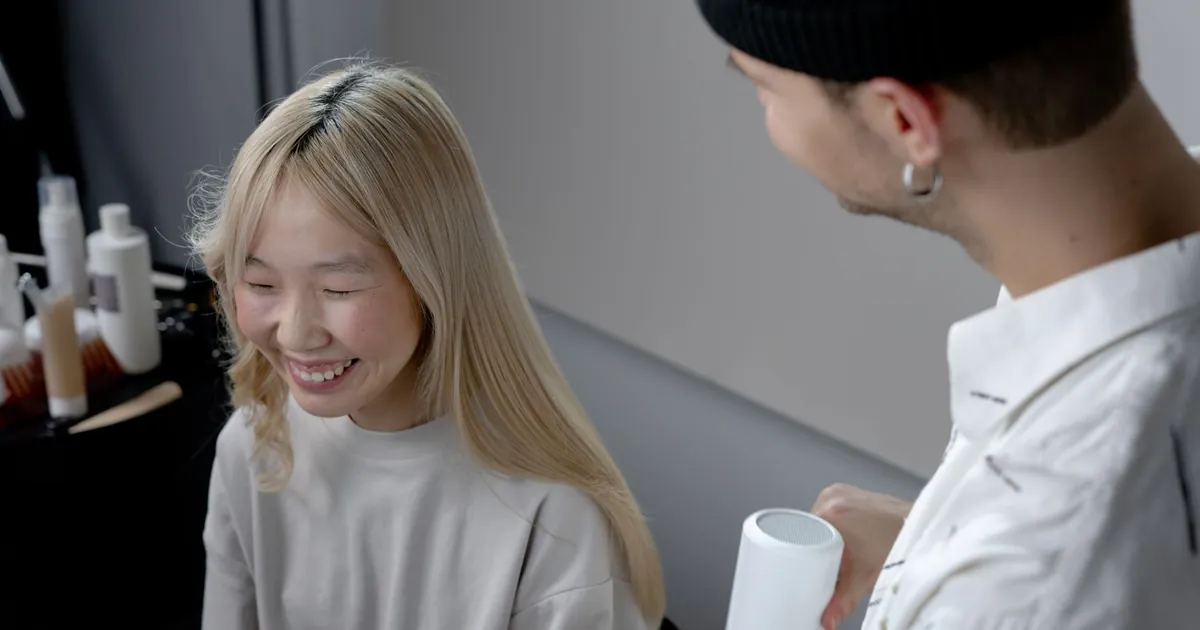 Une coiffeuse sèche les cheveux d'une femme souriante en salon de coiffure.