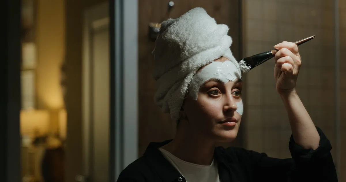 Femme appliquant un masque dans une salle de bain, serviette sur la tête