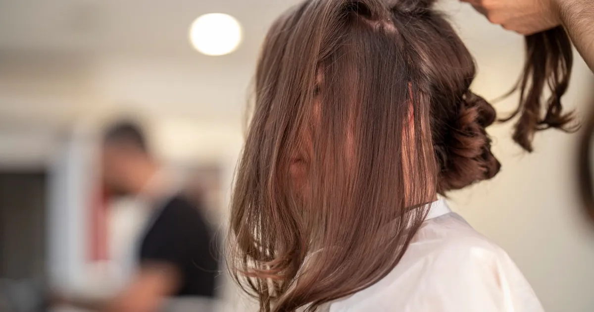 Vue de profil d'une femme dont les cheveux sont coiffés par une coiffeuse en salon moderne.