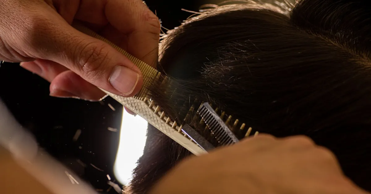 Gros plan sur un coiffeur coupant les cheveux avec un peigne et des ciseaux à l'intérieur.