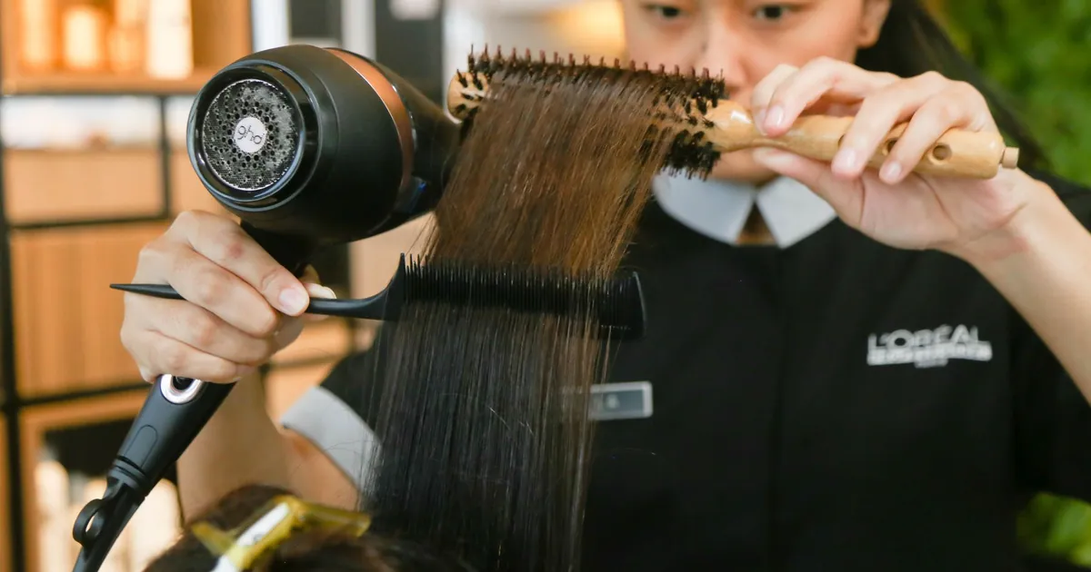 Une coiffeuse lisse des cheveux à la brosse et au sèche-cheveux dans un salon.