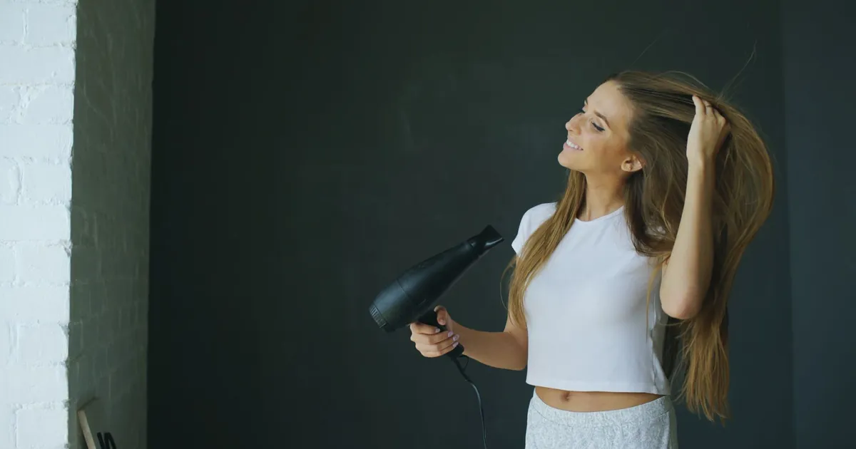 Jeune femme souriante utilisant un sèche-cheveux en intérieur