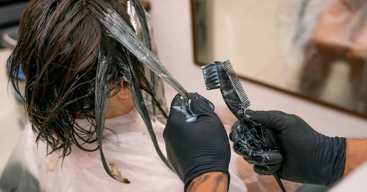 Gros plan d'une coloration en salon, coiffeur appliquant la teinture sur les cheveux.