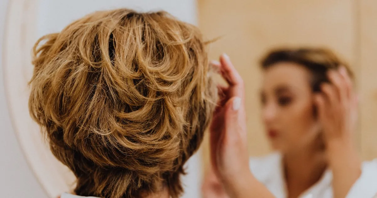 Femme de dos coiffant ses cheveux courts devant le miroir