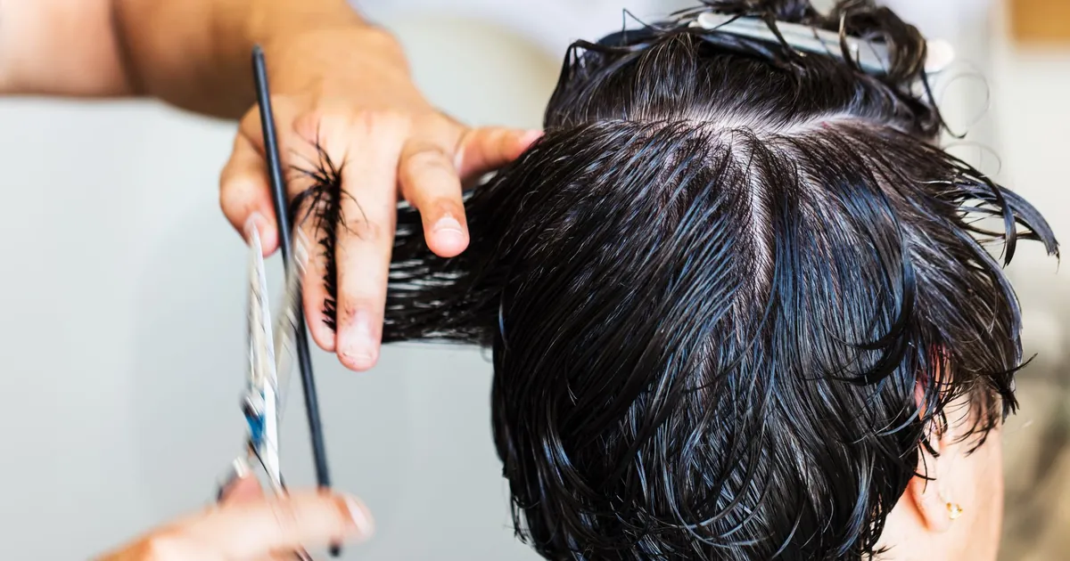 Coiffeuse coupant des cheveux mouillés foncés en salon