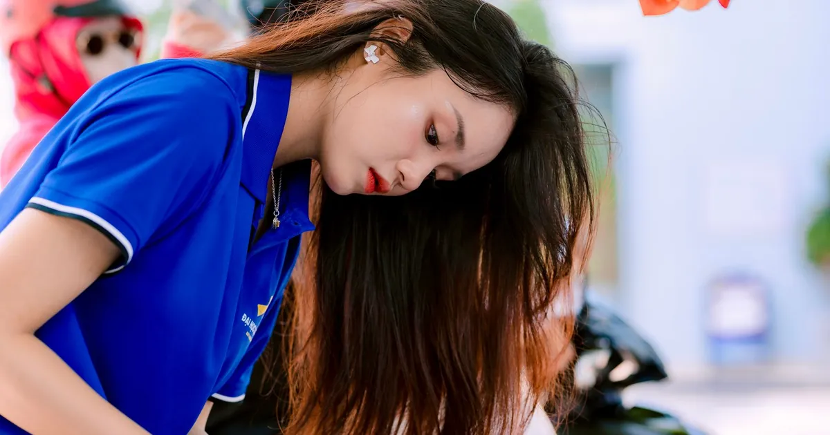 Jeune femme en polo bleu penchée, occupée à démêler ses longs cheveux dehors.