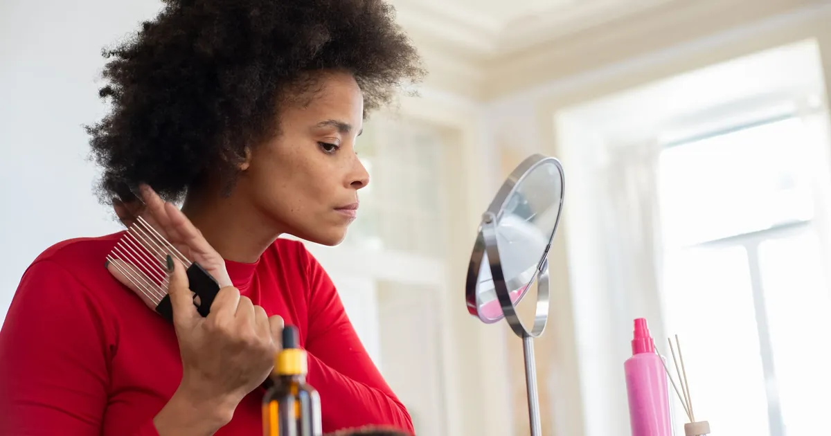 Femme en chemise rouge se coiffant devant un miroir de vanité, le matin.