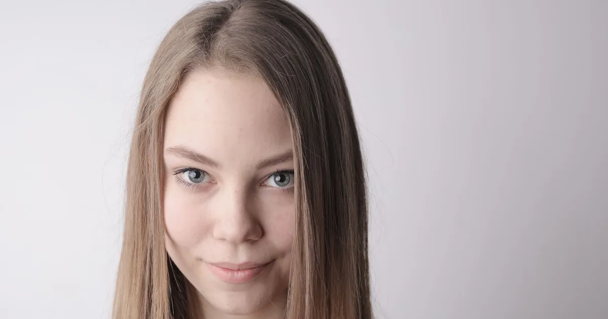 Portrait serré d'une jeune femme souriante au maquillage naturel et cheveux lisses.