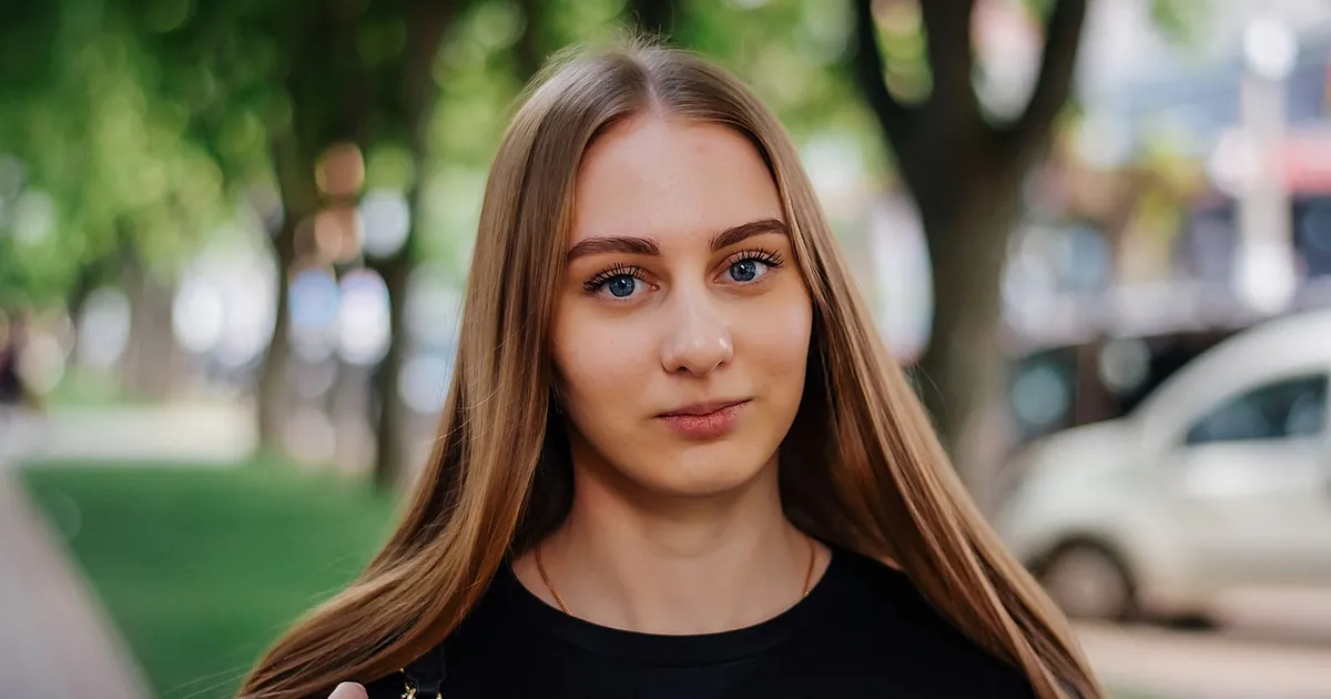 Portrait d'une jeune femme caucasienne aux longs cheveux blonds dans un parc ensoleillé.