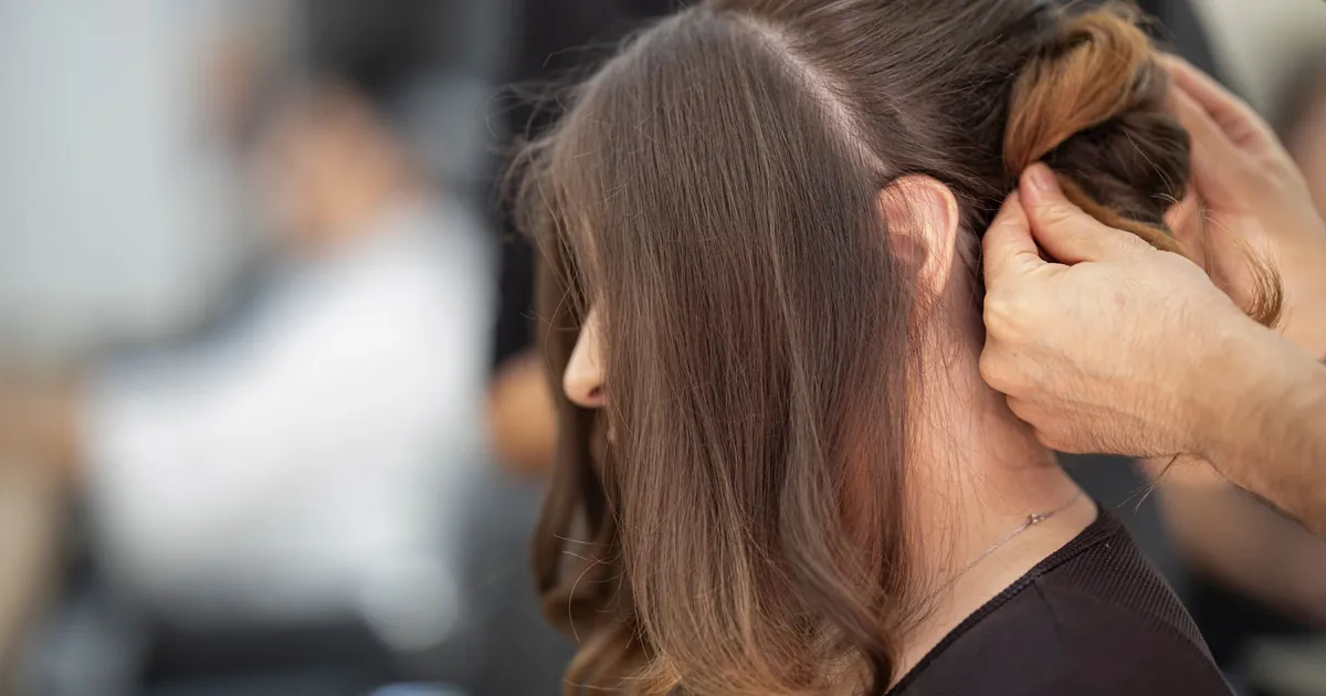 Gros plan sur une coiffeuse réalisant une coiffure élégante pour une femme en salon.