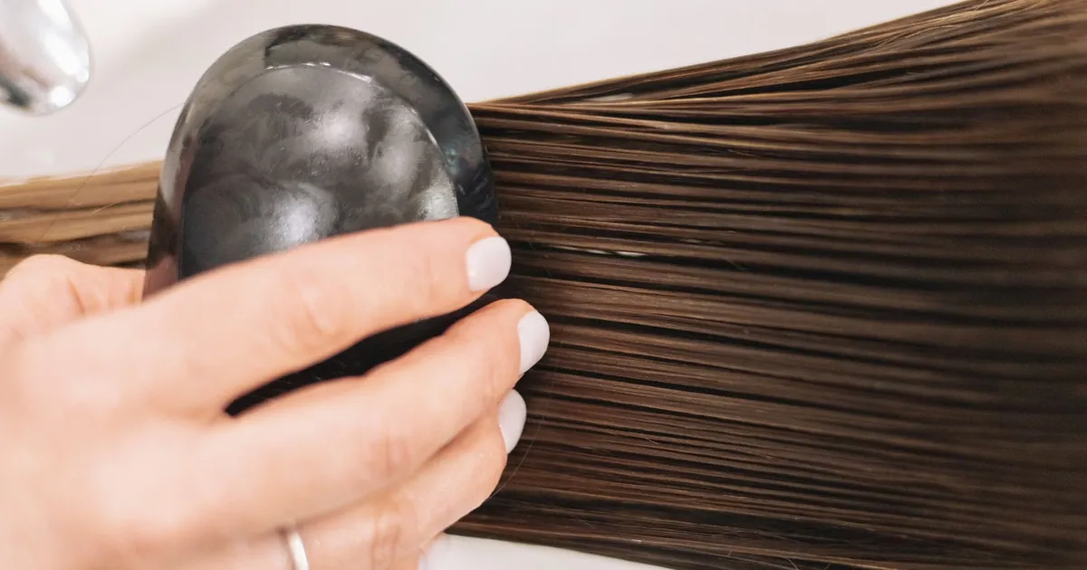 Gros plan d'une femme brossant ses longs cheveux bruns avec une brosse noire.