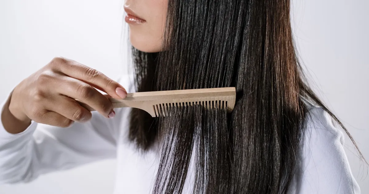 Gros plan d'une femme peignant ses cheveux avec un peigne en bois à l'intérieur.