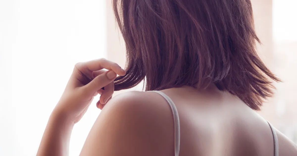 Dos et épaules d'une femme en lumière douce, main dans ses cheveux