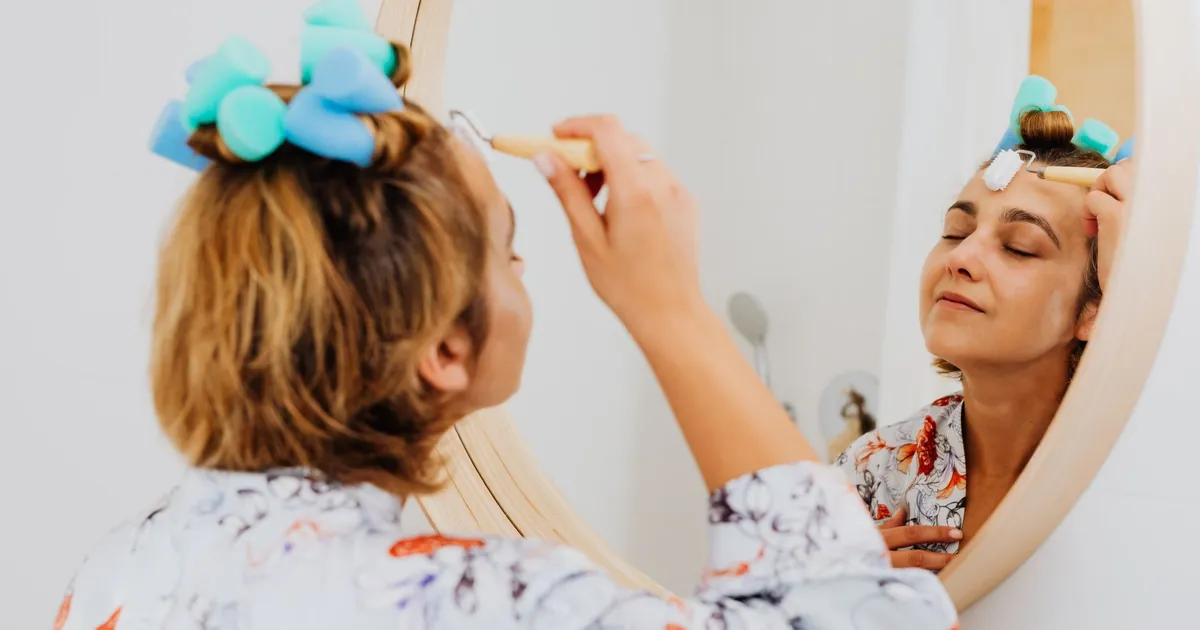 Femme aux yeux fermés appliquant un soin devant le miroir, moment de détente