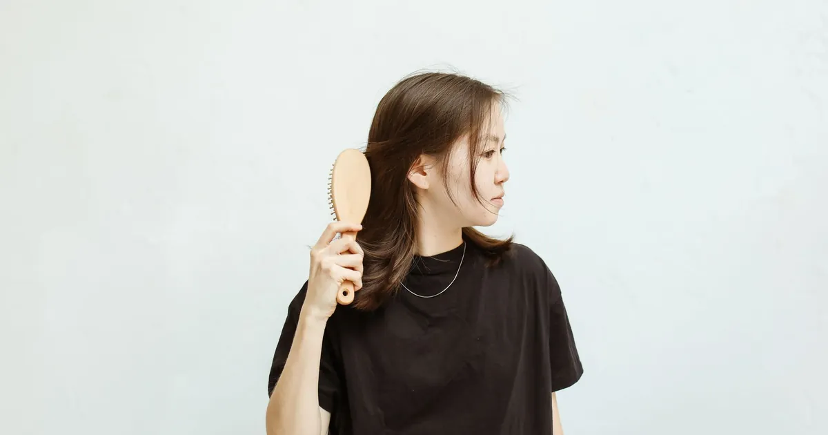 Jeune femme en chemise noire qui peigne ses cheveux sur fond blanc.