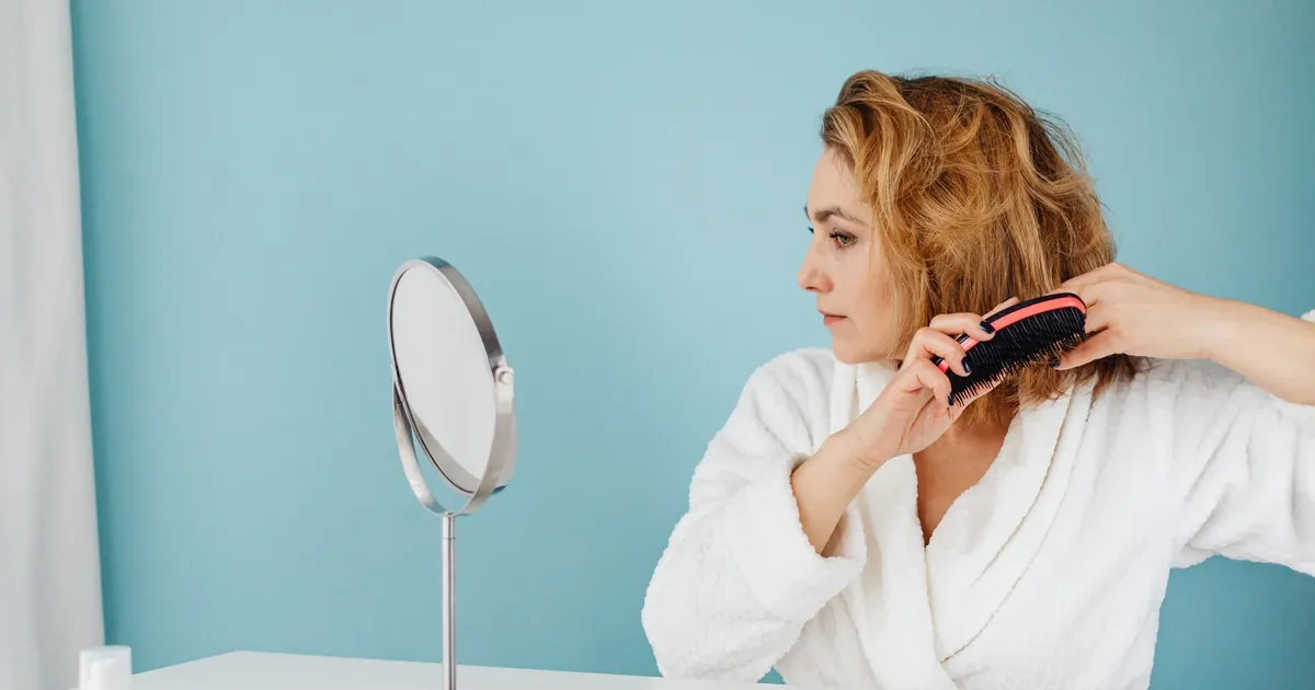Femme en peignoir se coiffant devant un miroir, routine matinale paisible.