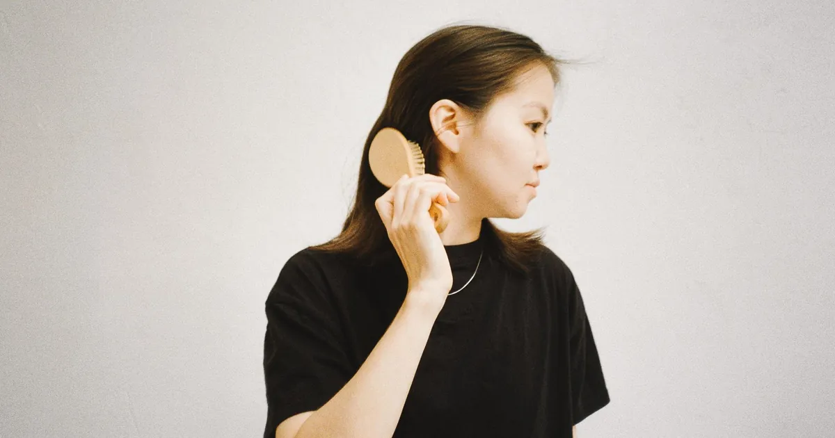 Femme asiatique en chemise noire se brossant les cheveux sur fond neutre.