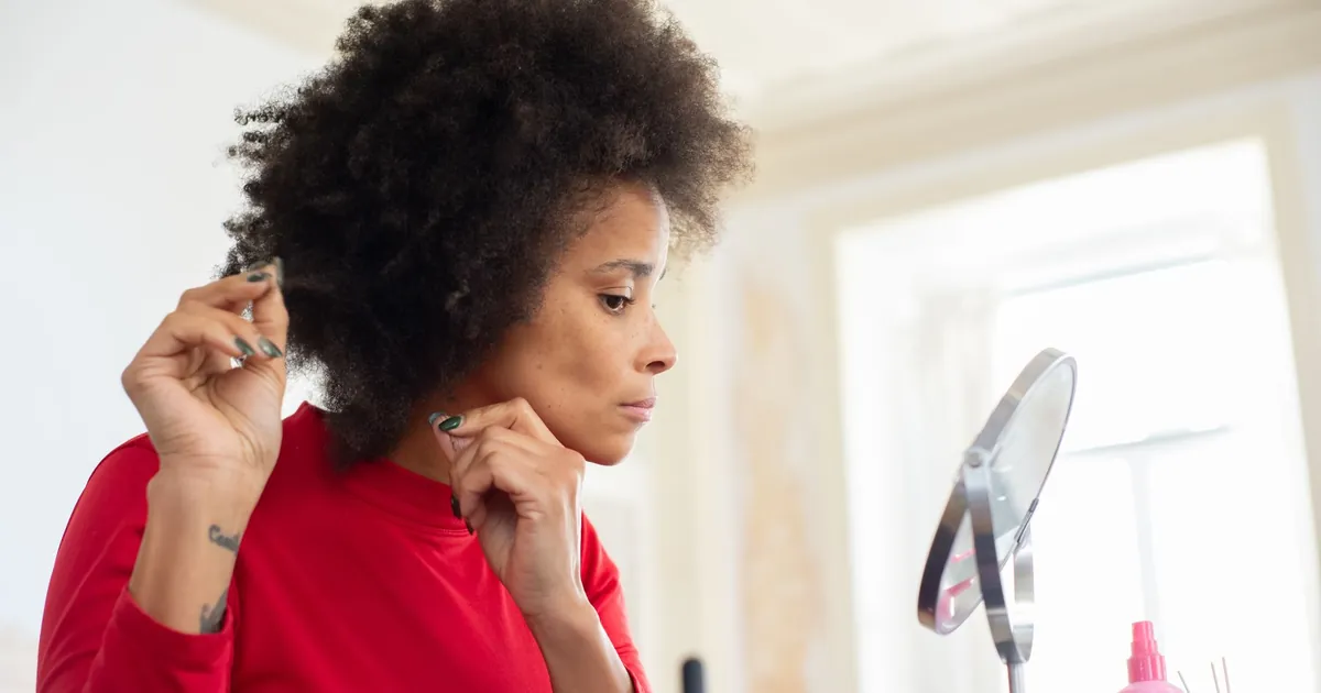 Femme aux cheveux afro se coiffant devant un miroir dans une pièce bien éclairée.