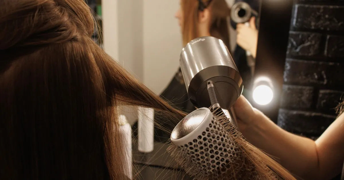 Coiffeuse séchant les cheveux d'une cliente au pistolet et à la brosse en salon