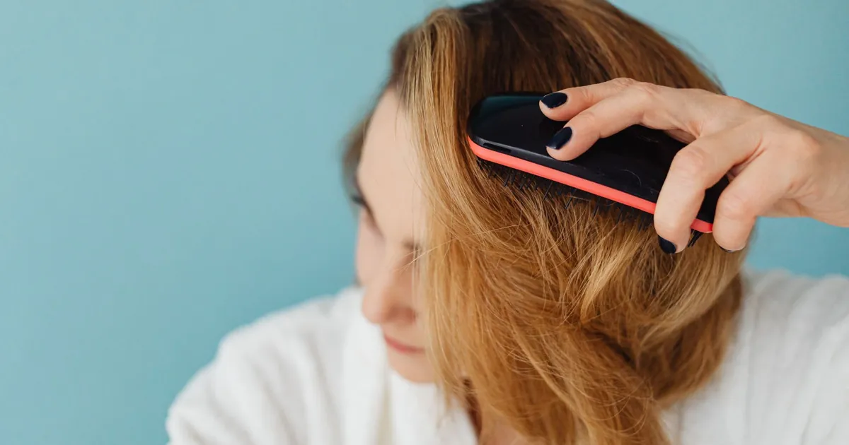 Gros plan d'une femme aux cheveux bruns se brossant les cheveux en peignoir.