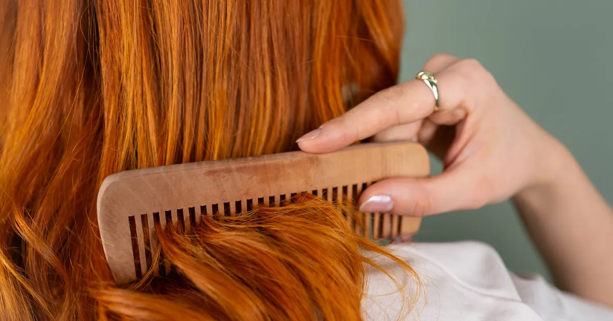 Gros plan d'une femme peignant ses longs cheveux roux avec un peigne en bois.