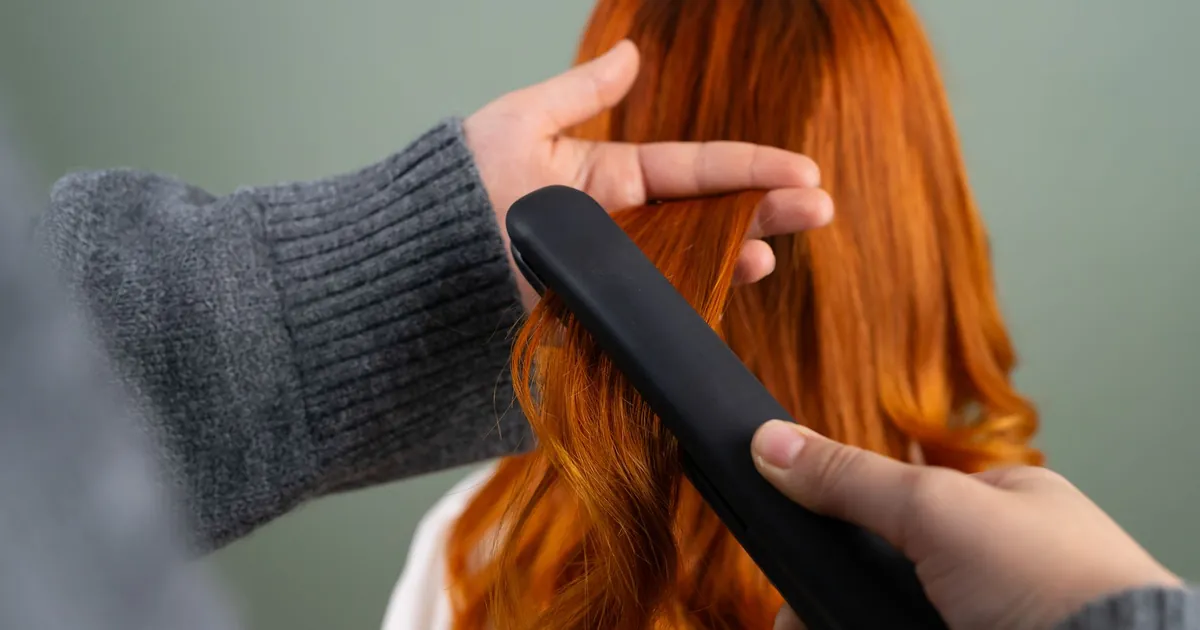 Mains lissant de longs cheveux roux au fer plat en intérieur