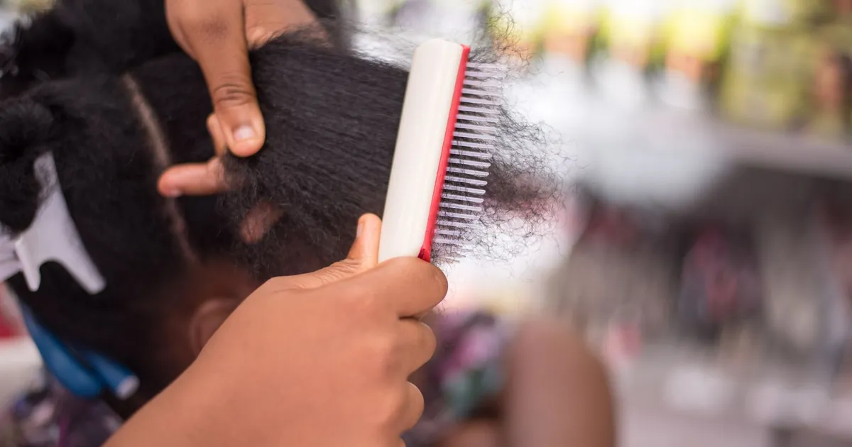 Gros plan sur une personne coiffant des cheveux afro, geste de soin et de coiffure.