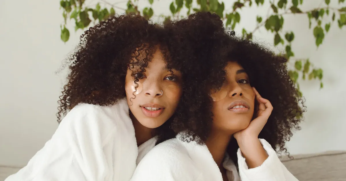 Deux femmes aux cheveux afro en peignoirs blancs se détendent à l'intérieur.