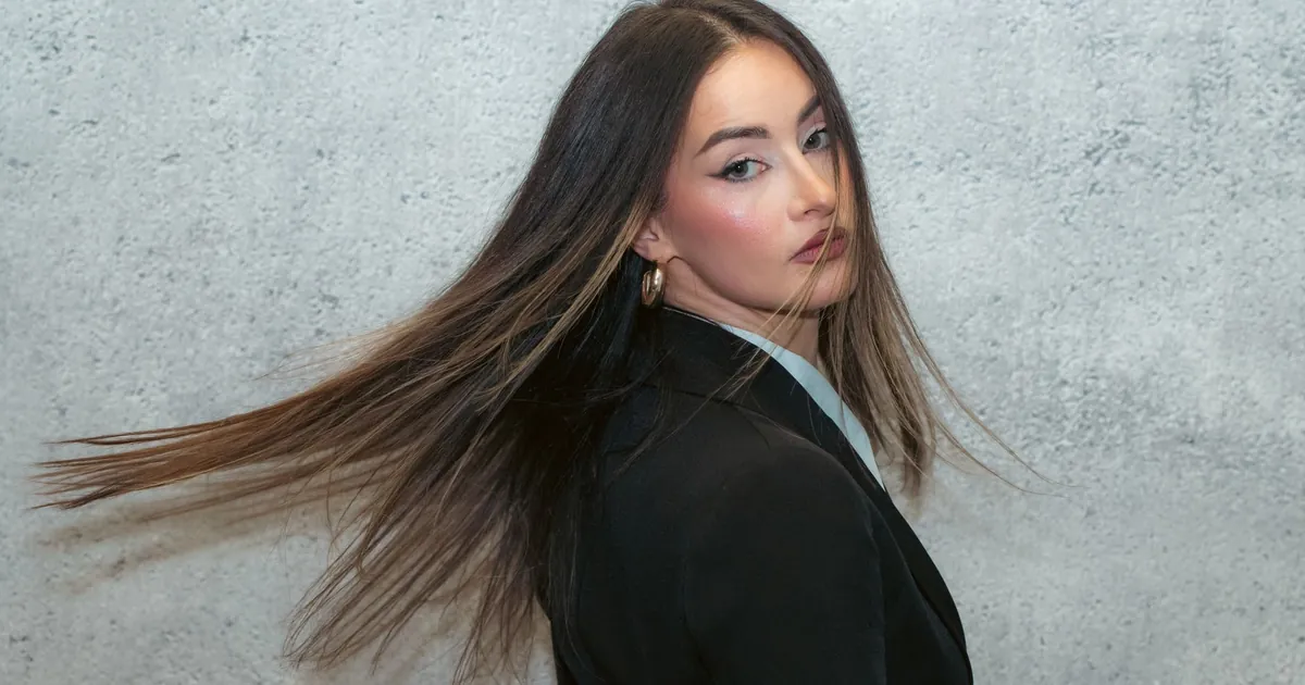 Femme élégante en blazer noir, cheveux fluides, fond texturé