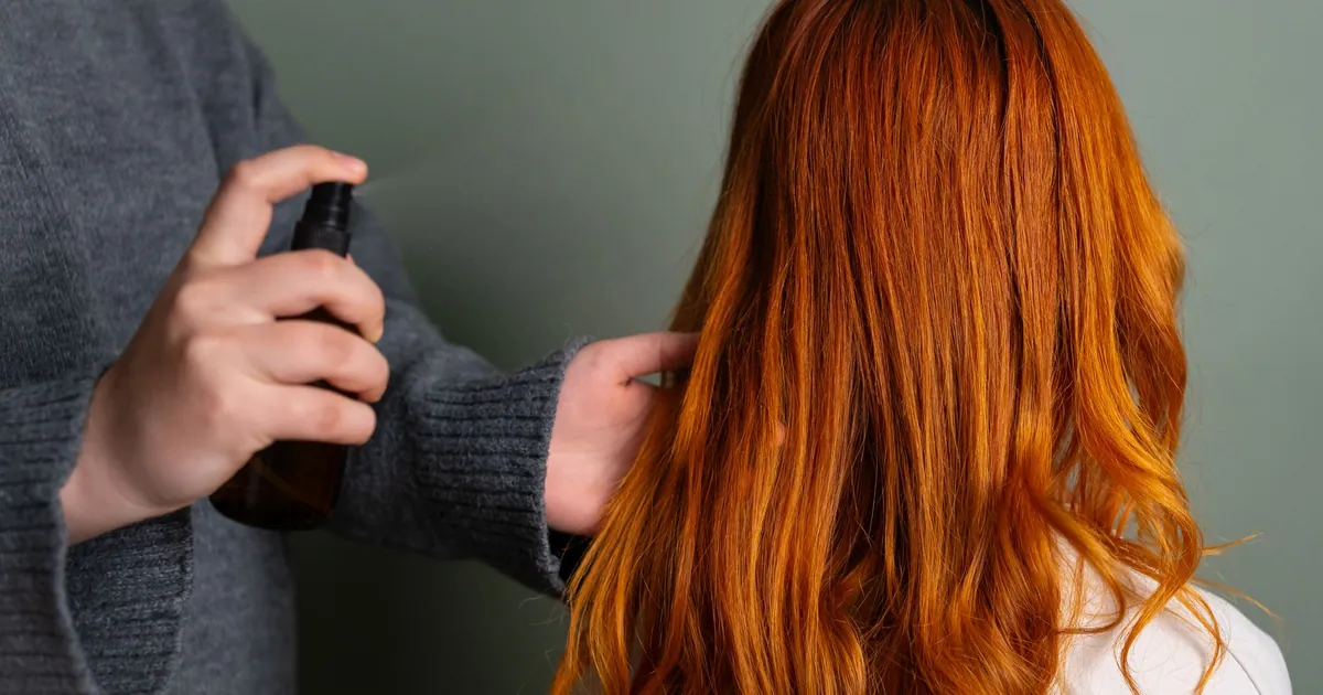 Gros plan d'un coiffeur vaporisant un produit sur de longs cheveux roux