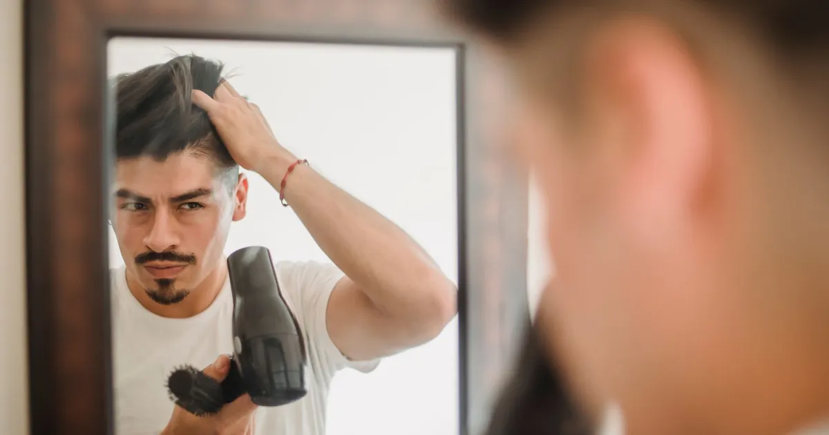 Homme adulte se coiffant au sèche-cheveux en regardant son reflet, routine moderne.