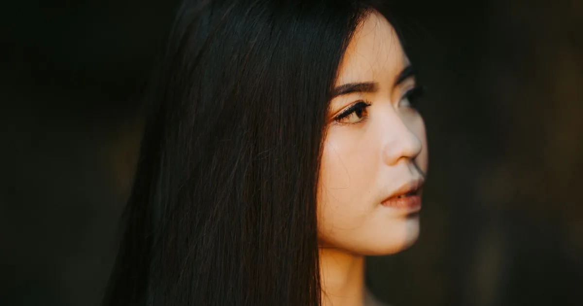 Portrait serré d'une jeune femme aux longs cheveux lisses, lumière douce, expression sereine.