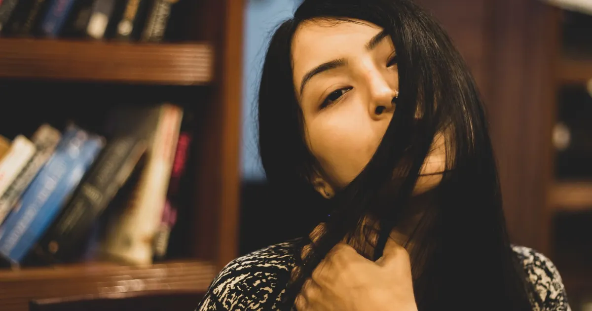 Jeune femme pensive aux longs cheveux, installée dans une bibliothèque cosy.