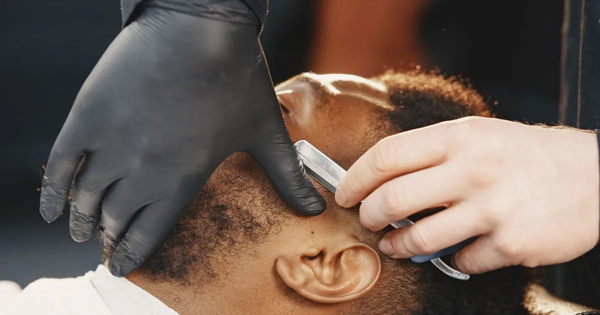 Un barbier rase la barbe d'un client au rasoir, geste précis et appliqué.