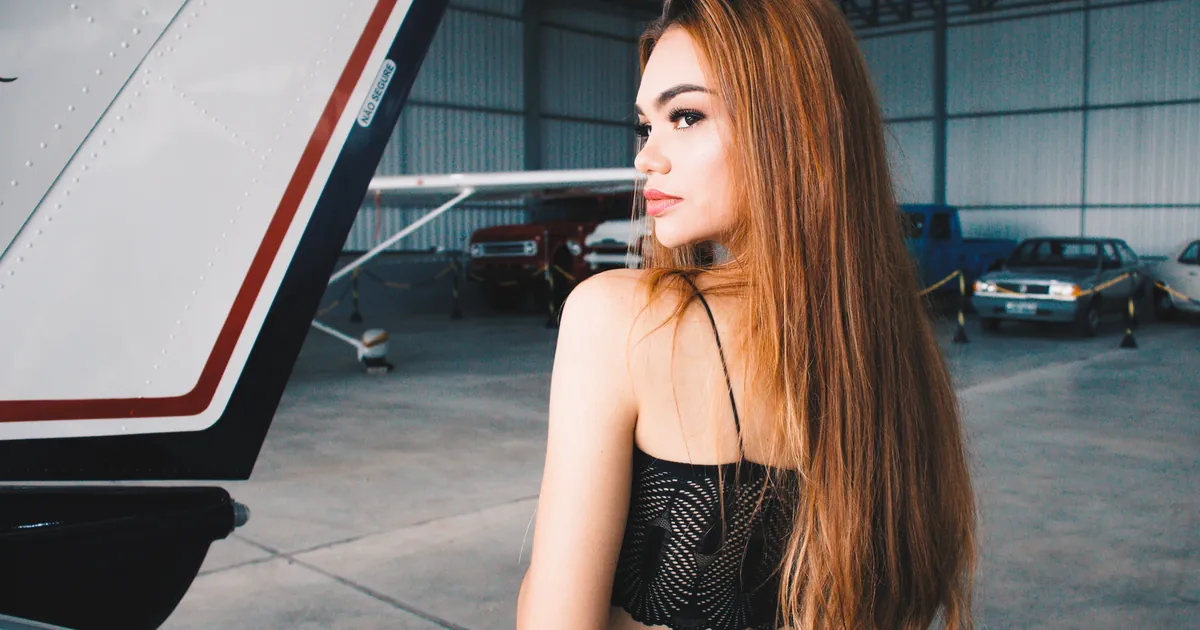 Femme aux longs cheveux pose près d'une aile d'avion dans un hangar