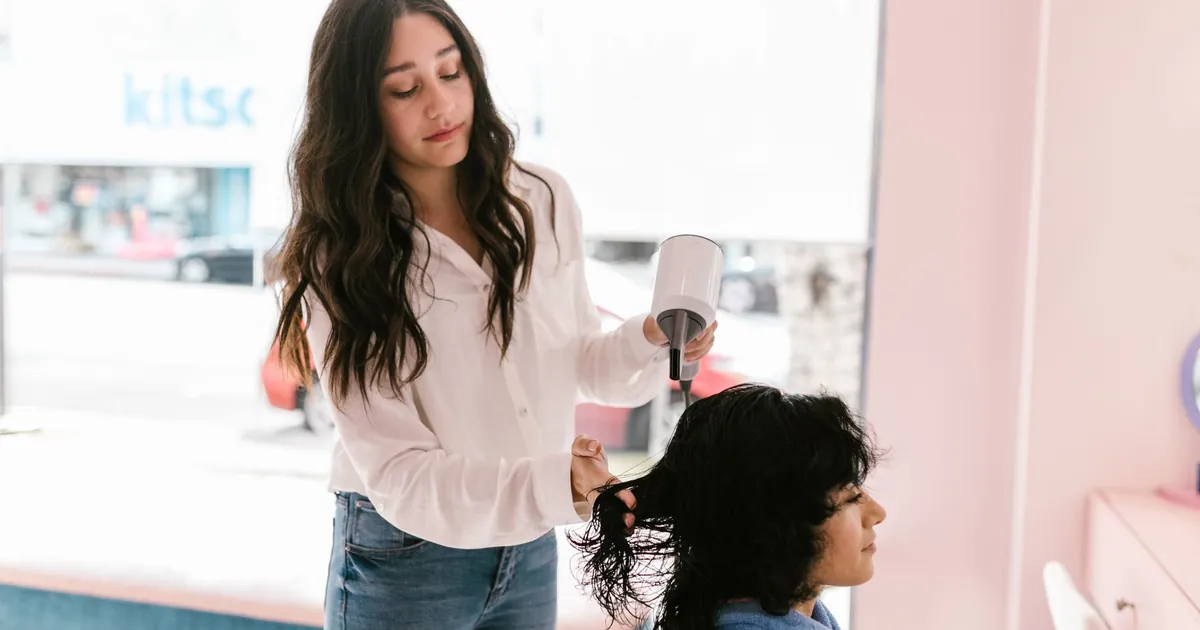 Coiffeur séchant les cheveux d'une cliente dans un salon moderne, ambiance professionnelle soignée