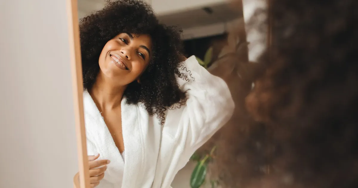 Femme souriante aux cheveux bouclés en peignoir chez elle