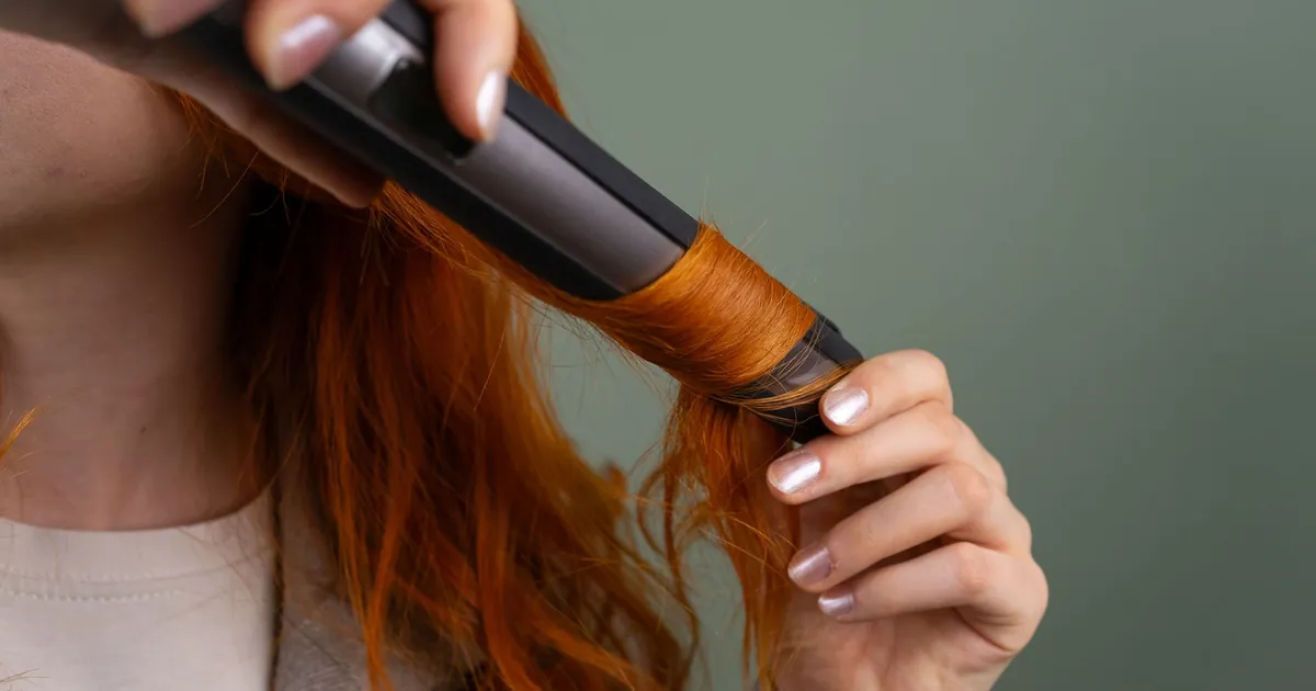 Gros plan sur une femme bouclant ses cheveux roux avec un fer à boucler.