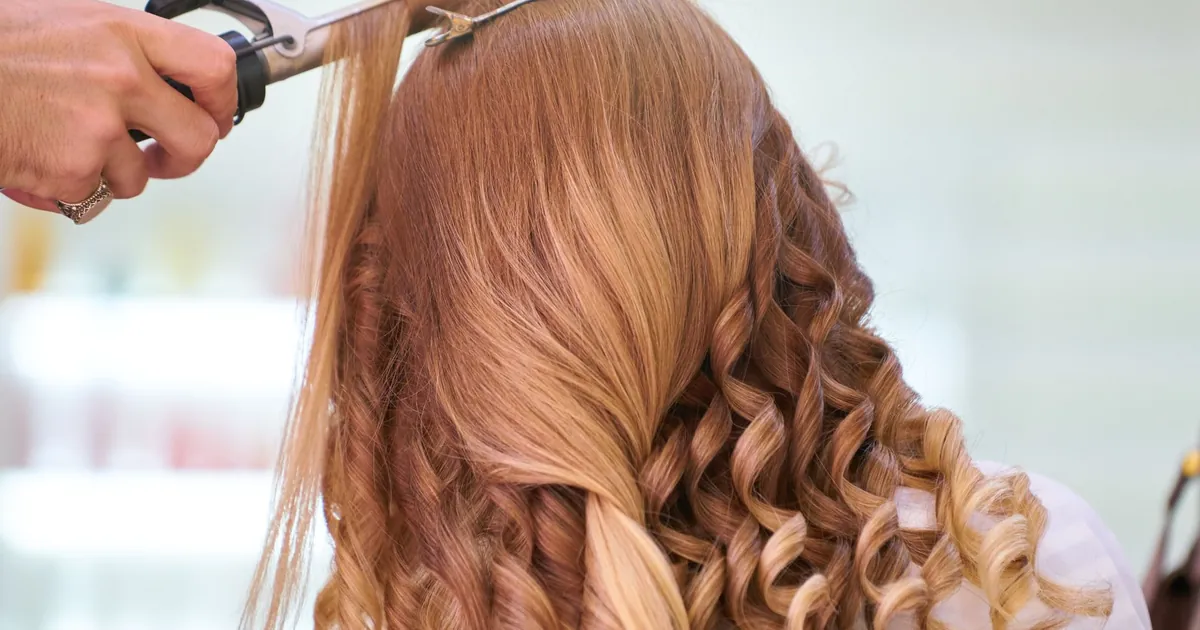 Gros plan sur une coiffeuse bouclant des cheveux blonds en boucles glamour dans un salon.