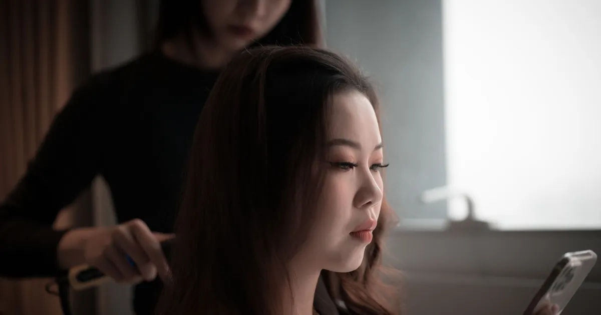 Femme asiatique sur son téléphone pendant qu'un coiffeur la coiffe.