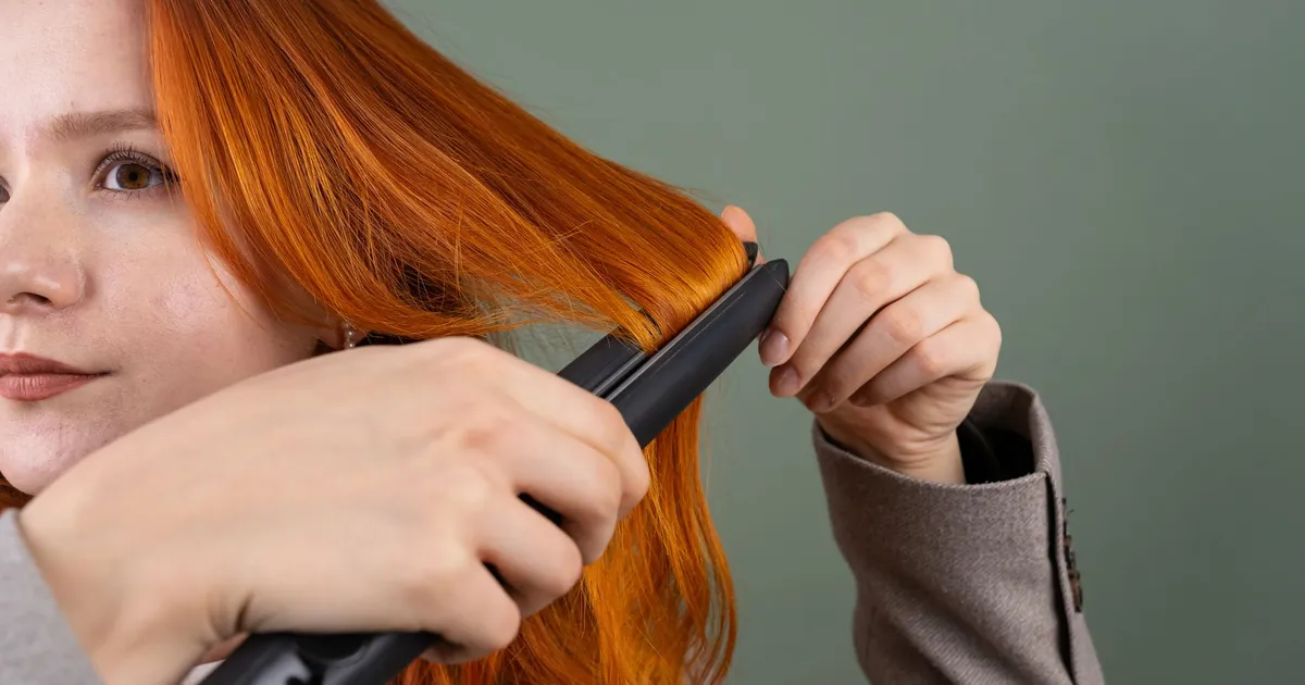 Gros plan d'une femme lissant ses cheveux roux, fond vert.