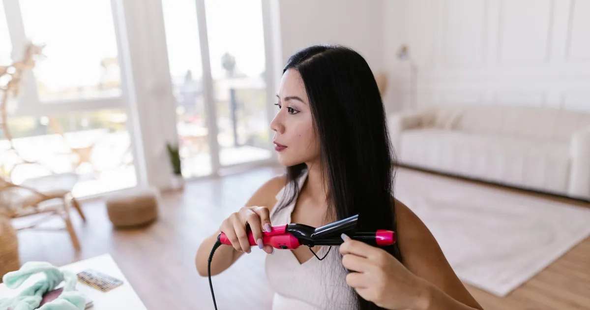 Une femme utilise un lisseur chez elle pour obtenir des cheveux lisses.