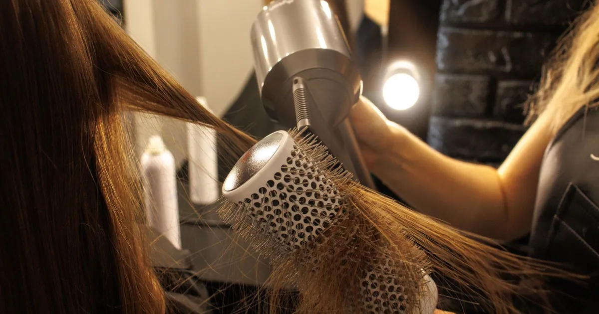 Coiffeur séchant et coiffant de longs cheveux à la brosse ronde en salon.